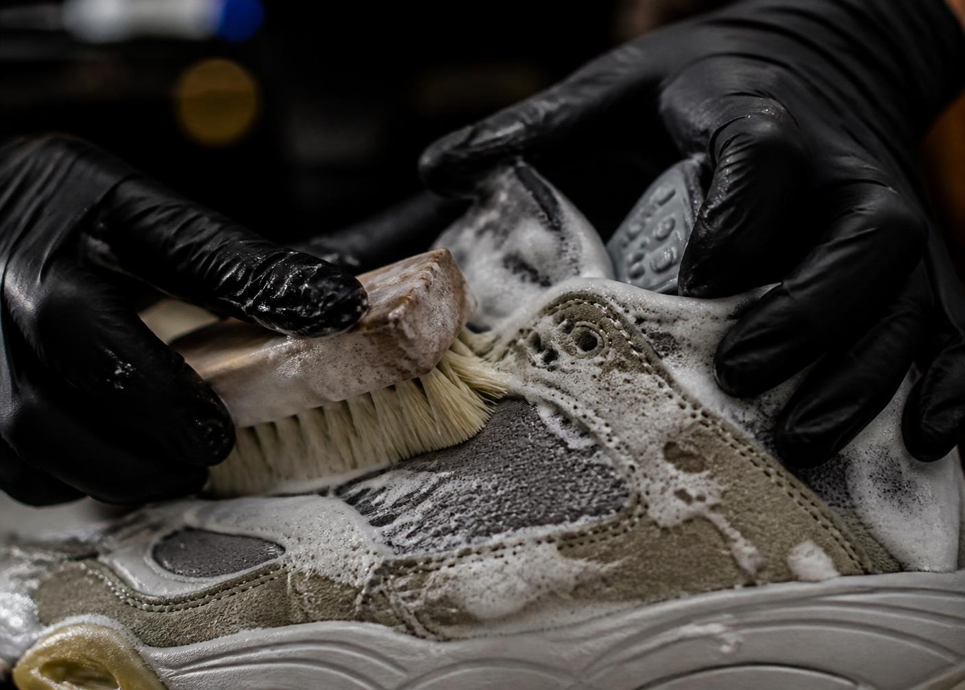 Gloved hands scrubbing foam into a sneaker upper